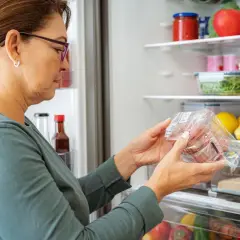Kvinna kollar på köttförpackning i kylskåpet, undrar hur länge håller paj i kylen.