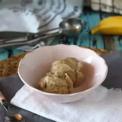 Två skopor krämig bananglass i en rosa skål. En banan ligger i bakgrunden, perfekt för ett enkelt bananglass recept.