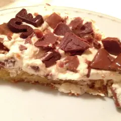 En bit krämig daim tårta med chokladbitar och en chokladdekoration.