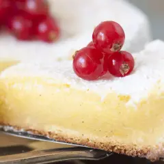En bit av en gul kaka med pudersocker och röda vinbär. Perfekt för ett vit choklad recept.