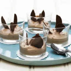 Fyra glas med len choklad dessert, dekorerade med chokladflarn, står på en turkos bricka. En perfekt avslutning på middagen.