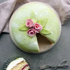 En grön prinsesstårta med rosa rosor och blad, perfekt för prinsesstårtans dag. En bit är uppskuren.