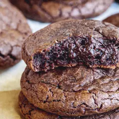 En hög med kladdkake cookies, en är uppäten och visar den sega, chokladiga insidan. Perfekt för fikat!