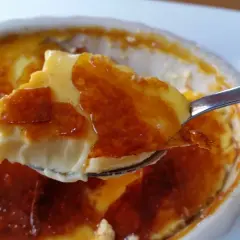 En sked tar en bit av en krämig creme brulee med knäckig karamell.