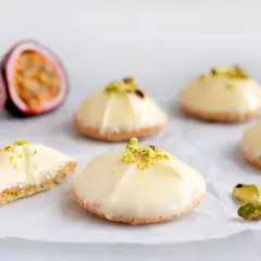 Små, vita bakelser med pistagecrunch, inspirerade av passionsfrukt recept. En är uppskuren och visar en krämig fyllning.