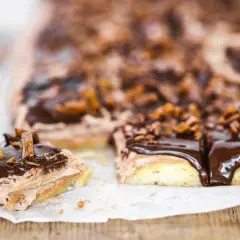 En bit av en chokladig snoddas kaka med fluffig kräm och chokladglasyr, toppad med krossad choklad och karamellbitar.