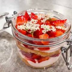 Strawberry and cream dessert layered in a glass jar, topped with fresh strawberries and small white flowers.