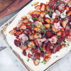 En generös prinsesstårta i långpanna, täckt med fluffig grädde, färska jordgubbar, örter och rosa blommor.