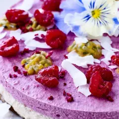 En vacker, rund kaka i rosa färg, dekorerad med hallon, passionsfrukt, kokosflingor och en blå viol.