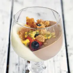 En vacker pannacotta tårta i glas med bär och smulor.