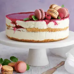 En vacker nyårstårta med lager av krämig fyllning, kexbotten och hallonspegel. Toppad med macarons, hallon och mynta. Ett perfekt nyårstårta recept!