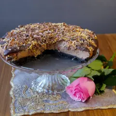 En läcker choklad cheesecake med chokladspån och nötter, serverad med en rosa ros.