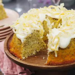 En saftig citron och vallmokaka med fluffig glasyr och citronskal. En bit är upplagd på en tallrik bredvid.