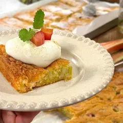 En bit saftig rabarberkaka i långpanna toppas med fluffig grädde och mynta. Perfekt till fikat!