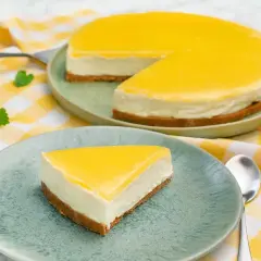 En krämig cheesecake med en syrlig lemon curd-topping. En bit serverad på en tallrik bredvid en hel cheesecake.