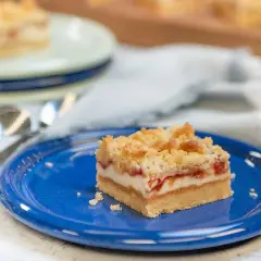 En bit rabarber cheesecake med smuldeg på en blå tallrik.