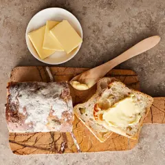 Bröd med smör på en skärbräda. En skål med smörskivor och en träsked. Vad kan man använda istället för smör? Kanske en god olivolja?