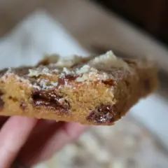 En hand håller en bit av ett blondie recept med chokladbitar.