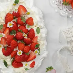 En vacker pavlova med vispgrädde och massor av saftiga jordgubbar, dekorerad med små vita blommor. Perfekt för en somrig fika.
