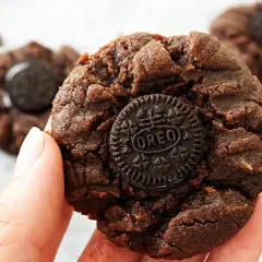 En hand håller en chokladkaka med en Oreo-kaka i mitten. Flera liknande nutella kakor syns i bakgrunden.