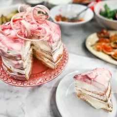 En vacker rabarberkompott tårta med rosa glasyr och dekorationer. En bit är upplagd på en tallrik.