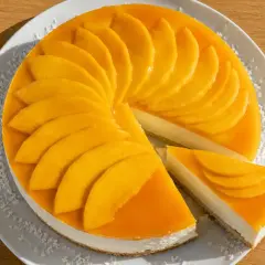 En krämig mango cheesecake med färska mangoskivor som pryder toppen. En bit är uppskuren och visar den vita fyllningen.