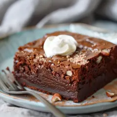 En bit fudgy brownie med hasselnötter och en klick grädde på en blå tallrik.
