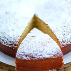 En saftig sockerkaka med yoghurt, pudrad med florsocker. En bit är uppskuren och redo att avnjutas.