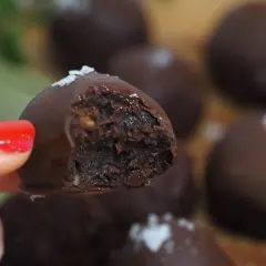 En hand med rött nagellack håller en chokladpralin med dadelfyllning. Perfekt för att baka med dadlar!