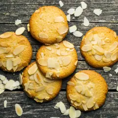 Små, gyllene mandelkakor, perfekta för ett bondkakor recept. Spridda mandelflagor på en rustik träyta.