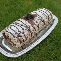 En läcker Budapest tårta, rullad och dekorerad med choklad och pudersocker, ligger på ett silverfat på gräsmattan.