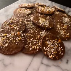 En hög med runda, mörka kakor med mandelmjöl och choklad, toppade med hackade nötter och pärlsocker. Perfekta till fikat!