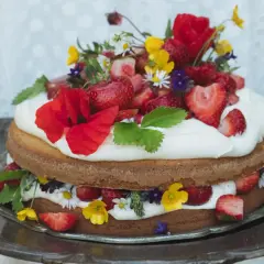 En vacker sommartårta med jordgubbar, grädde och vilda blommor på ett silverfat. Perfekt för en solig dag.