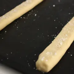 Två degstänger med flingsalt på en svart plåt, redo att bli ljuvliga kolakakor.