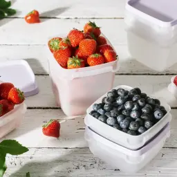 Färska jordgubbar, blåbär och hallon i plastburkar redo att frysa in. Perfekt för att bevara sommarens smaker.
