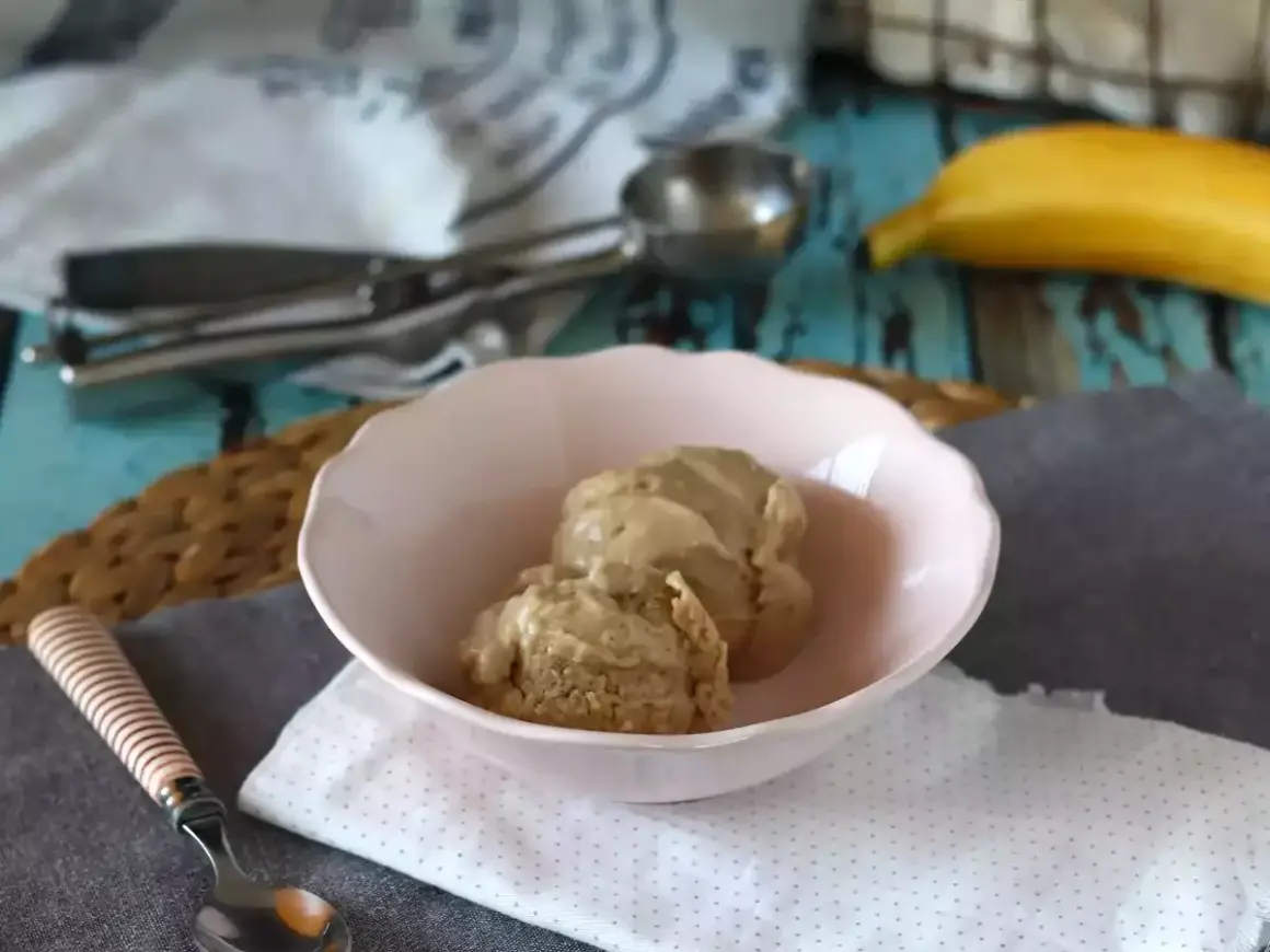 Två skopor krämig bananglass i en rosa skål. En banan ligger i bakgrunden, perfekt för ett enkelt bananglass recept.