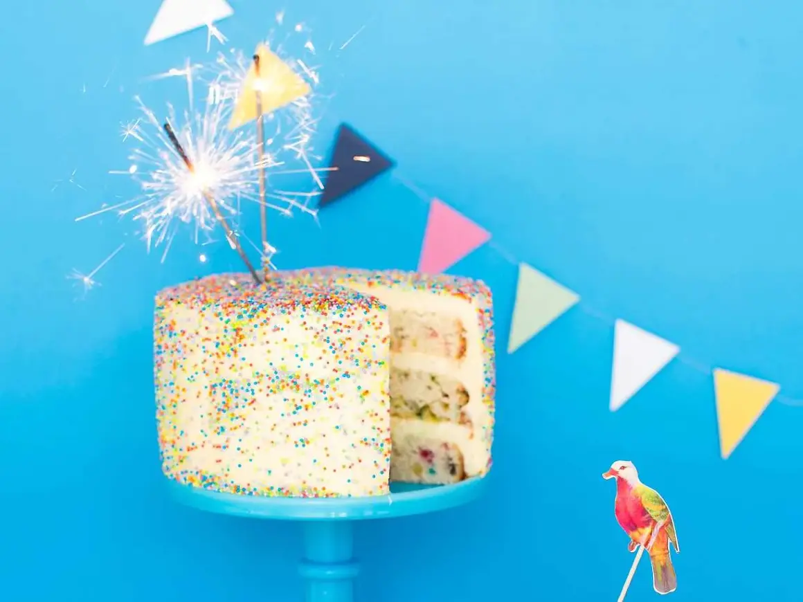 En festlig funfetti tårta med stjärnljus och en färgglad fågeldekoration. Perfekt för ett kalas!