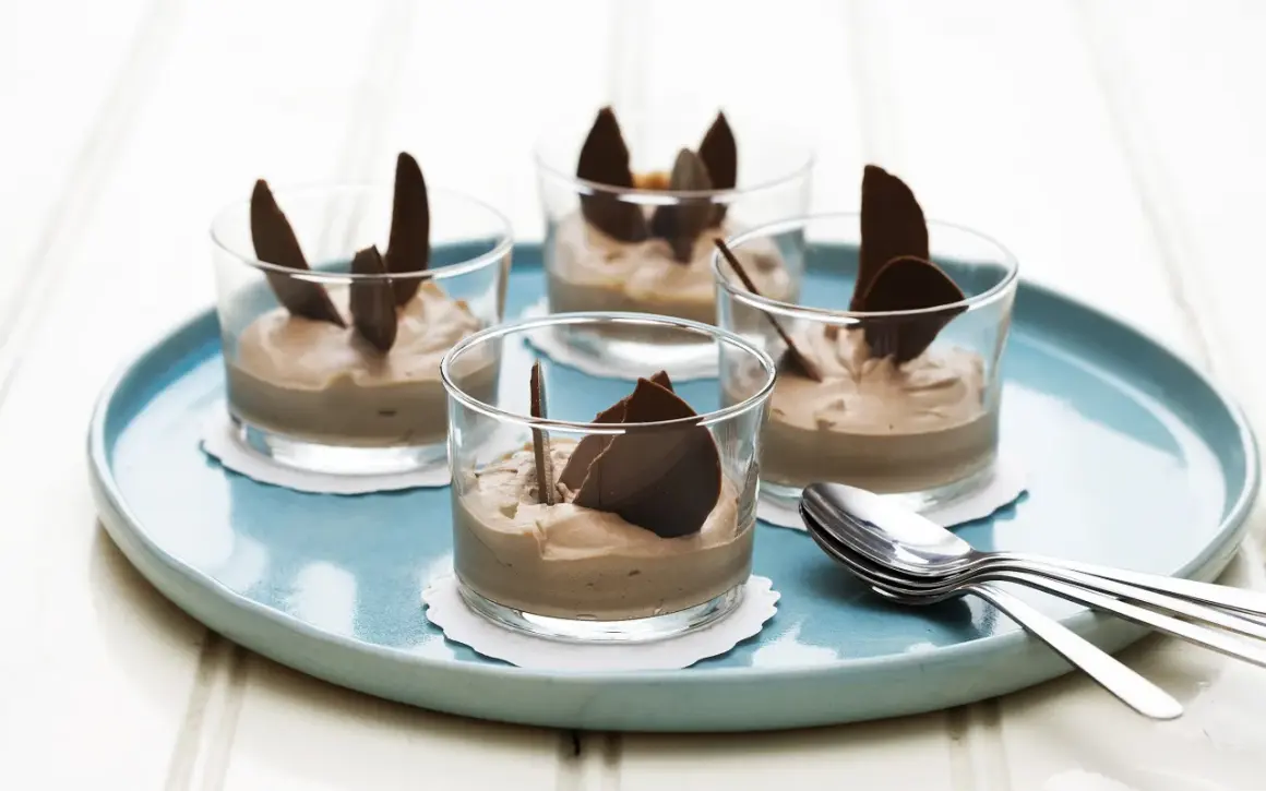 Fyra glas med len choklad dessert, dekorerade med chokladflarn, står på en turkos bricka. En perfekt avslutning på middagen.
