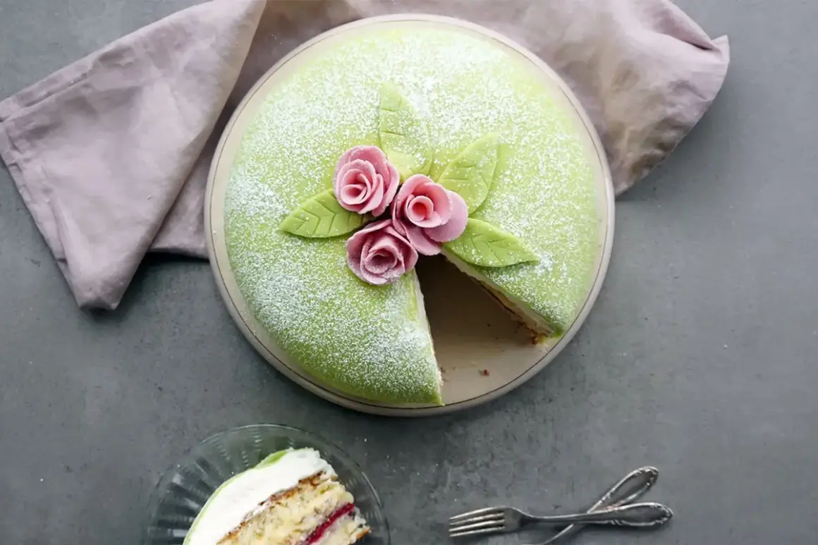 En grön prinsesstårta med rosa rosor och blad, perfekt för prinsesstårtans dag. En bit är uppskuren.