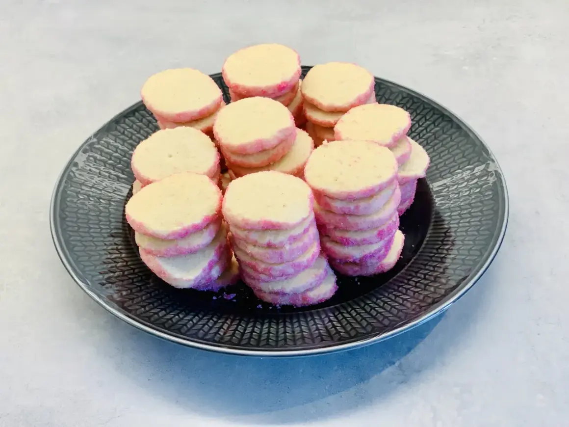 En hög med hembakade brysselkex med rosa sockerkanter ligger på en mörk tallrik. Perfekt för fikat!