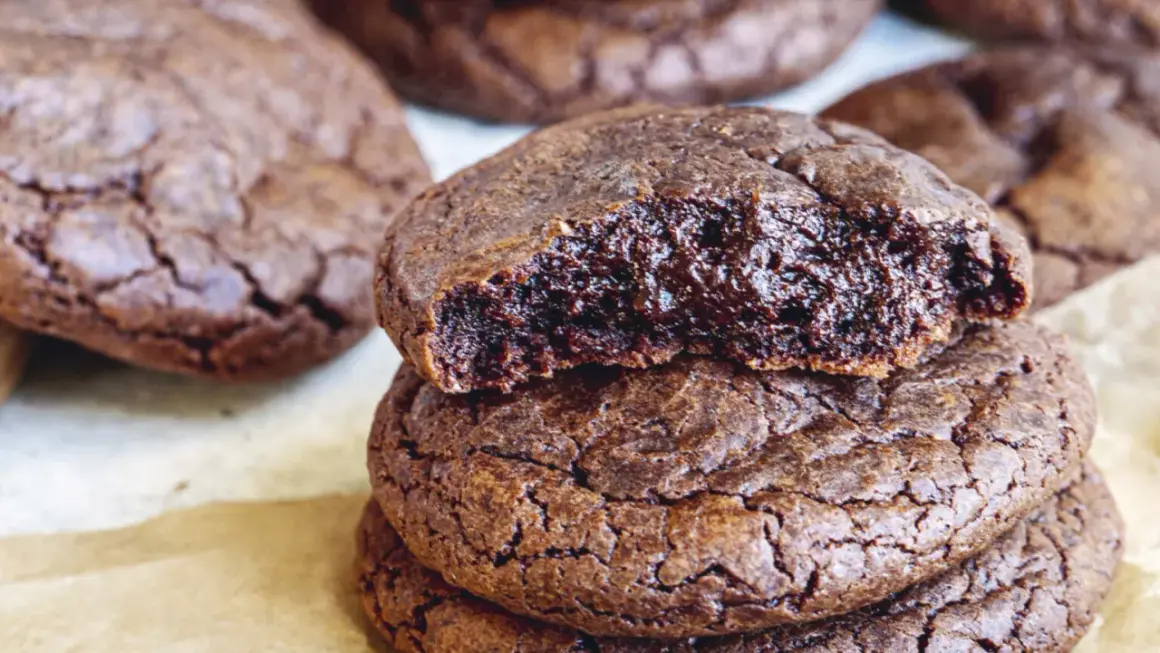En hög med kladdkake cookies, en är uppäten och visar den sega, chokladiga insidan. Perfekt för fikat!
