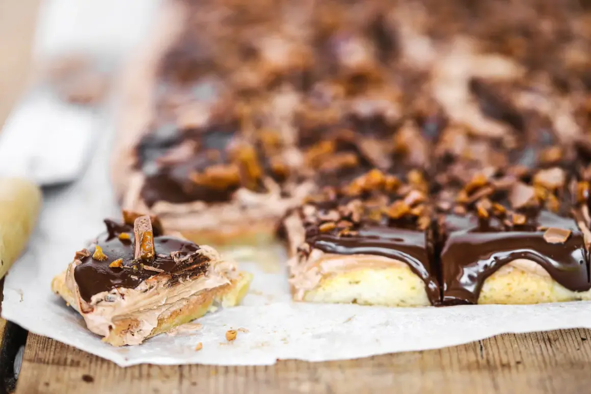 En bit av en chokladig snoddas kaka med fluffig kräm och chokladglasyr, toppad med krossad choklad och karamellbitar.