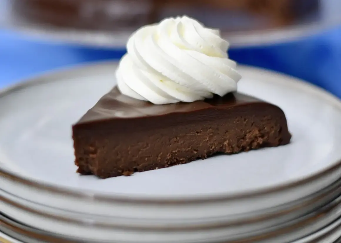 A slice of rich chocolate cake topped with whipped cream on a white plate.