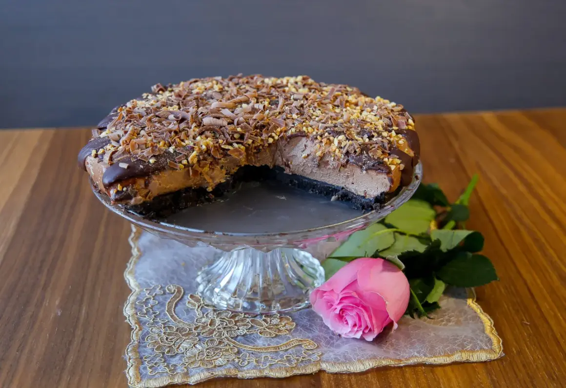 En läcker choklad cheesecake med chokladspån och nötter, serverad med en rosa ros.
