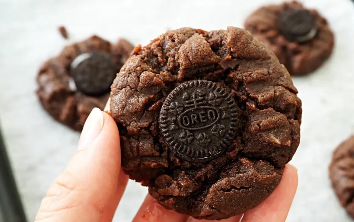 En hand håller en chokladkaka med en Oreo-kaka i mitten. Flera liknande nutella kakor syns i bakgrunden.