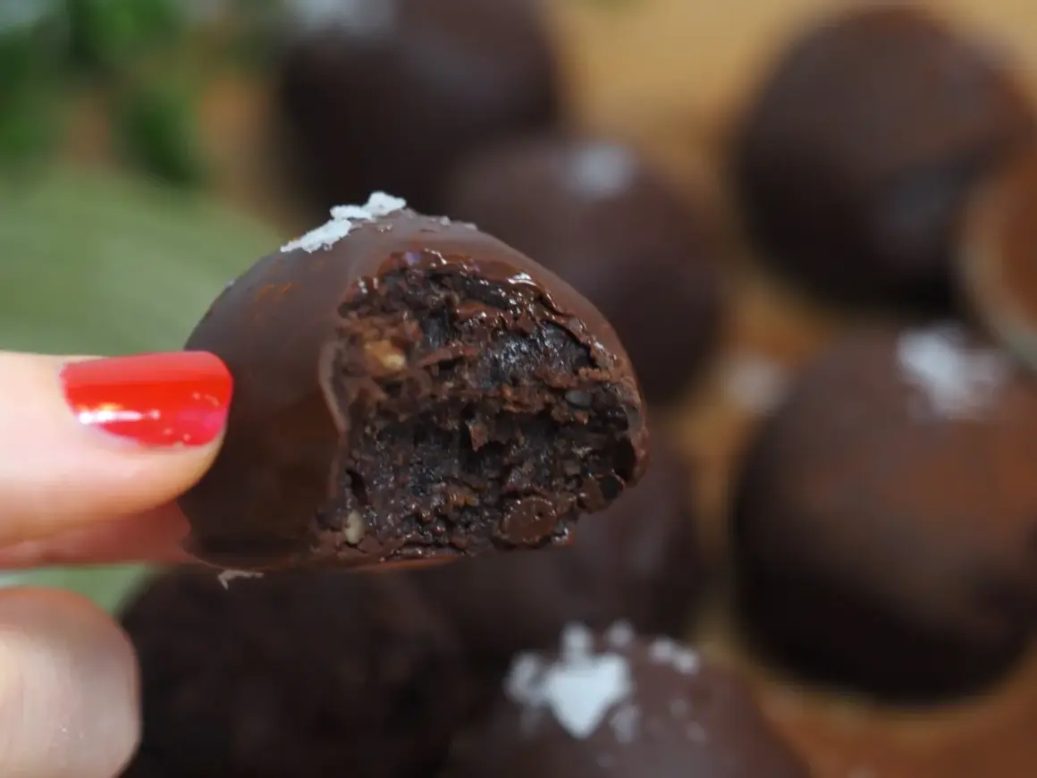 En hand med rött nagellack håller en chokladpralin med dadelfyllning. Perfekt för att baka med dadlar!