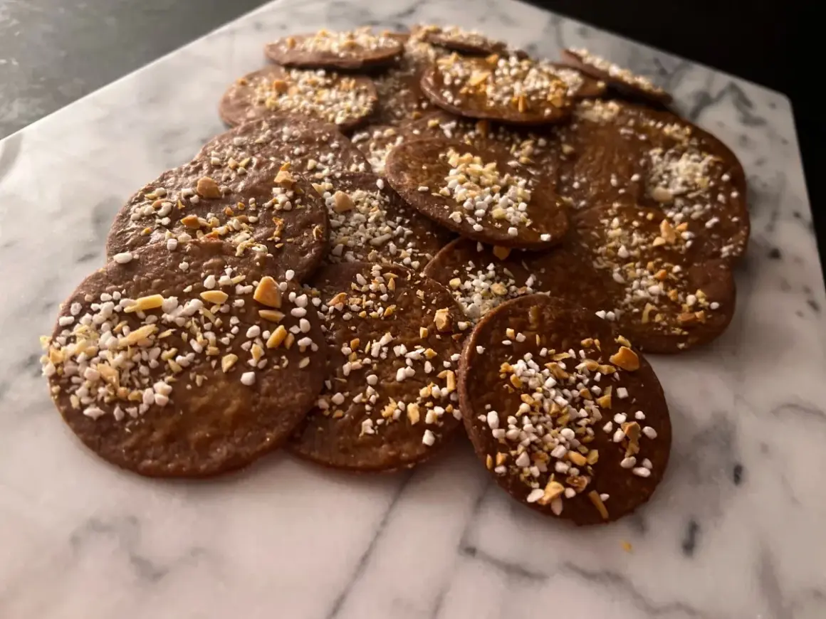 En hög med runda, mörka kakor med mandelmjöl och choklad, toppade med hackade nötter och pärlsocker. Perfekta till fikat!