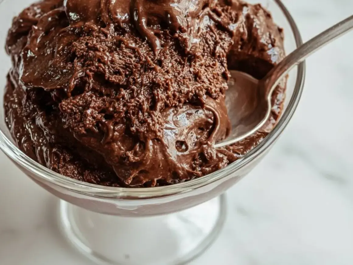 En sked tar en tugga av krämig chokladmousse i en glasskål. Perfekt för ett enkelt chokladmousse recept.