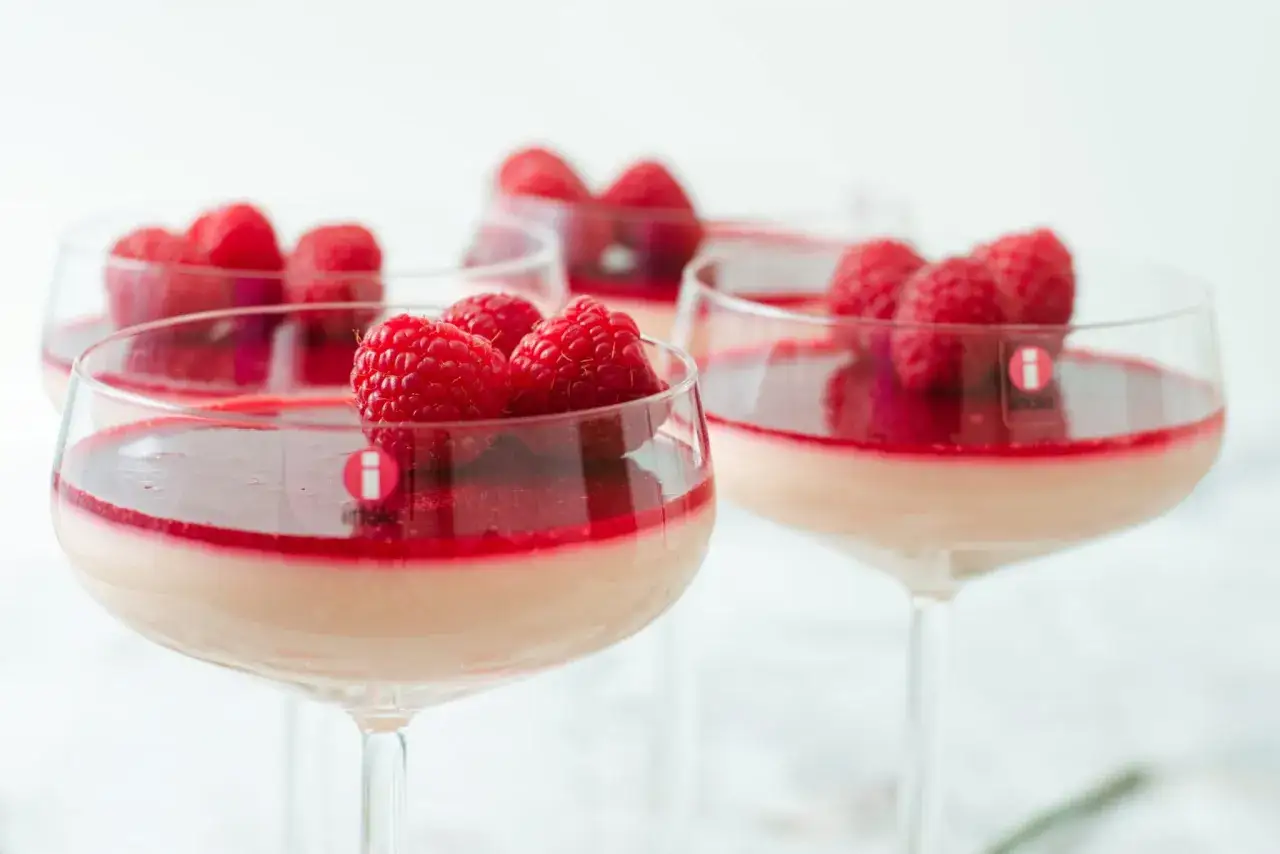 Flera glas med krämig panna cotta toppad med hallon och hallonsås. En perfekt dessert.