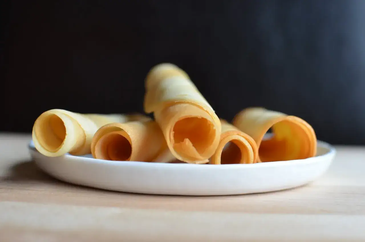 Krispiga rullade kex p&aring; en vit tallrik, perfekta f&ouml;r ett enkelt tuile recept.